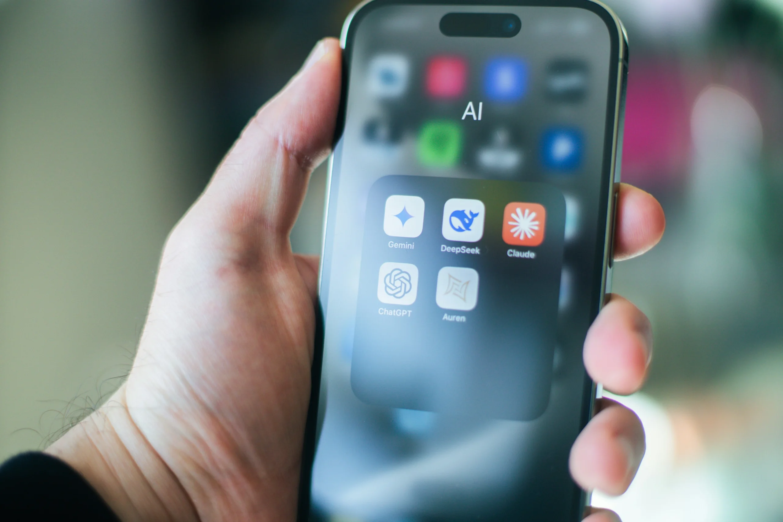 Iphone в руках людини на якому відкрита папка з інструментами ШІ(LLM): Клауд,Чат ГПТ, Діп Сік
